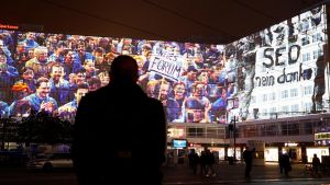 A silhouette of a person with footage from the fall of the Berlin Wall plays in the background