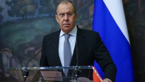 Russian Minister of Foreign Affairs Sergeĭ Lavrov stands at a podium in front of a Russian flag and painting.
