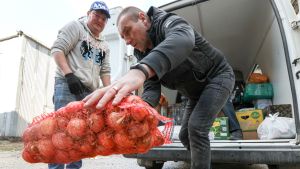 Two people holding big bag of onions, collecting humanitarian aid (water, food, hygiene products) for people evacuated from Donetsk and Lugansk People's Republics