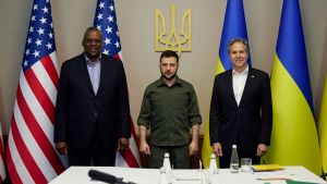 Lloyd Austin, Antony Blinken, and Volodomyr Zelenskyy before US and Ukraine flags.