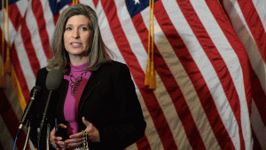Senator Joni Ernst giving speech in front of flag backdrop