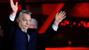 Viktor Orban raises his arms in front of a red background