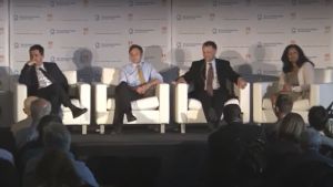 Four people sit in chairs on stage