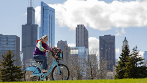 A woman rides a Divvy bike in front of the Chicago skyline.