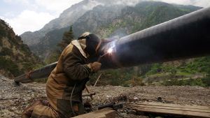 A welder works on a pipe with mountains in the background