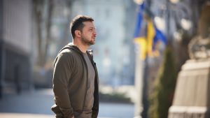 Ukrainian President Zelensky stands with a Ukrainian flag in the background