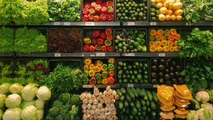 A shelf of vegetables is illuminated by fluorescent lighting in a grocery store.