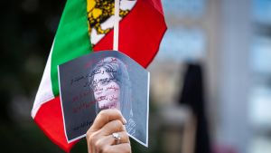 a person holds a photo of Mahsa Amini in the air at a protest 