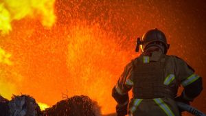 Fires are put out after air strikes in Ukraine, silhouetted firefighter against orange flames.