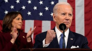 Biden pumping fist in front of a mic with Harris clapping behind him, American flag in the background.