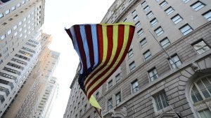 American flag with Ukraine flag colors in the white spots, blowing in the wind seen from below with skyscrapers behind.