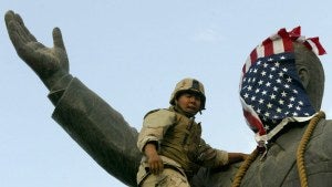 A Marine covers the face of a statue of Iraqi President Saddam Hussein with a US flag
