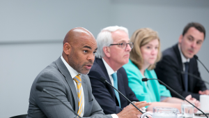 Three men and a woman sit at a conference desk. 