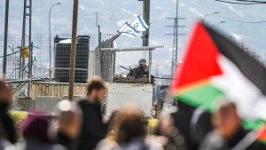 An Israeli soldier guards while Palestinians raise flags during a demonstration