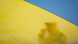 Silhouette of a soldier tipping their cap behind the yellow portion of a Ukrainian flag. 