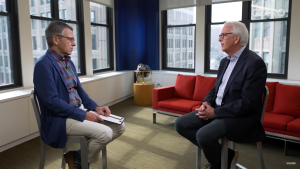 Ivo Daalder (R) and Ian Bremmer (L) sit facing each other on stools in front of a red couch and windows.