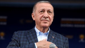 Turkish President Erdogan in a plaid suit with hand on heart in front of a microphone. 