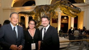 Three people stand in front of a dinosaur skeleton