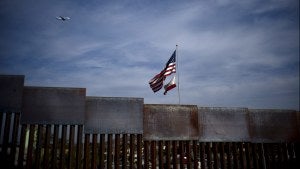 American and California state flags fly behind the US-Mexico border wall