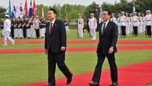 Kishida, right, and Yoon Suk Yeol, left, walk on a red carpet on green grass before troops.