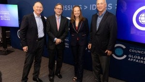 Sarah Gilbert stands with three members of the Council board including John Ettelson near blue background and two TV monitors. 