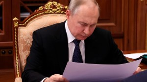 Putin looks down at paper and frowns, seated in ornate chair.