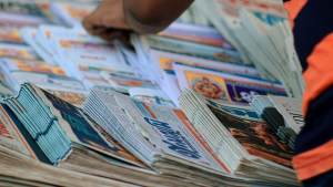 A hand selects from a stack of newspapers.
