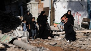 Adults in black garments carry kids near rubble in Gaza. 