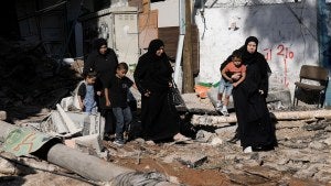 Adults in black garments carry kids near rubble in Gaza.