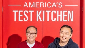 Two people in front of a red wall with "American's Test Kitchen" written across it