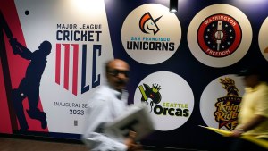In-motion image of a person walking in front of a wall listing professional cricket teams