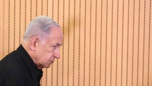 Benjamin Netanyahu seen in profile before a light brown paneled background.