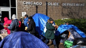 Asylum-seekers are served food within a small tent community outside a North Side police station.