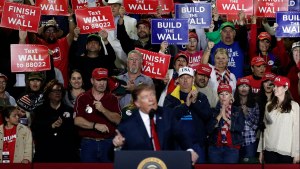 People hold signs that say finish the wall as Donald Trump speaks at a rally