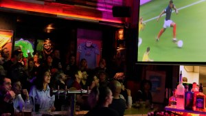 People sit around a bar, watching soccer on a TV