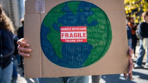 a person holds a poster of the Earth that says handle with care