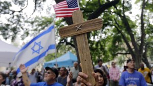 a wooden cross held in front of American and Israeli flags