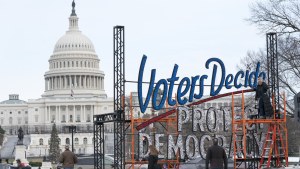  With the US Capitol in the background, people walk past a sign that says Voters Decide Protect Democracy