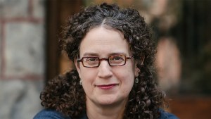 Headshot of a woman with curly dark hair and glasses