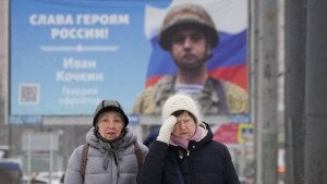 Women walk past a billboard with a portrait of a Russian soldier awarded for action in Ukraine and the words Glory to the heroes of Russia