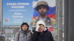 Women walk past a billboard with a portrait of a Russian soldier awarded for action in Ukraine and the words Glory to the heroes of Russia