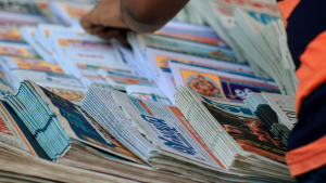 A hand selects from a stack of newspapers.