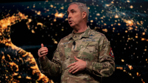 General Stephen N. Whiting speaks in front of a screen showing a close-up photo of Earth from space.