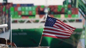 A US flag is shown in front of a container ship at the Port of Los Angeles