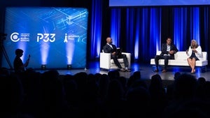 Three people sit in chairs on a stage in front of a crowd