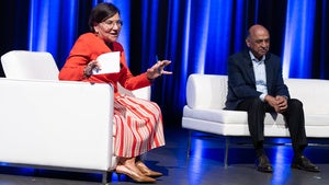 Two people sit on stage in white chairs