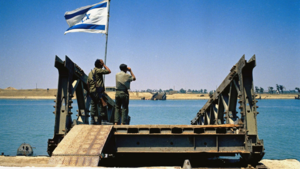 Two soldiers stand at a destroyed bridge, holding the Israeli flag