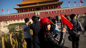 A woman holds a Chinese flag as she poses for a photo near Tiananmen Gate