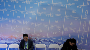 Men sit near a periodic table showing minerals at the China International Supply Chain Expo in Beijing on November 27, 2024.