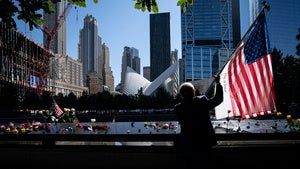 a man holds an American flag near the National September 11 Memorial and Museum